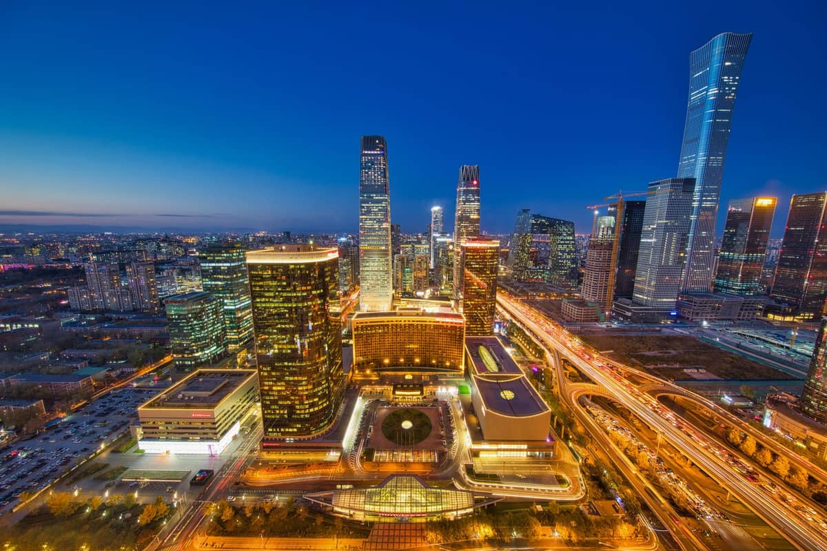 Luftaufnahme von Beijings zentralem Geschäftsviertel in der Dämmerung mit gitterartigen Straßen, modernen Wolkenkratzern und beleuchteten Highways.