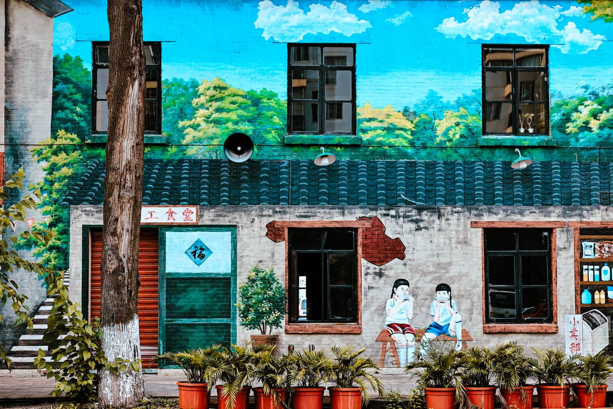 Buntes Wandgemälde an einem Fabrikgebäude, bemalt mit Bäumen, Himmel und zwei Personen, passend zur künstlerischen Atmosphäre des 798 Art District.