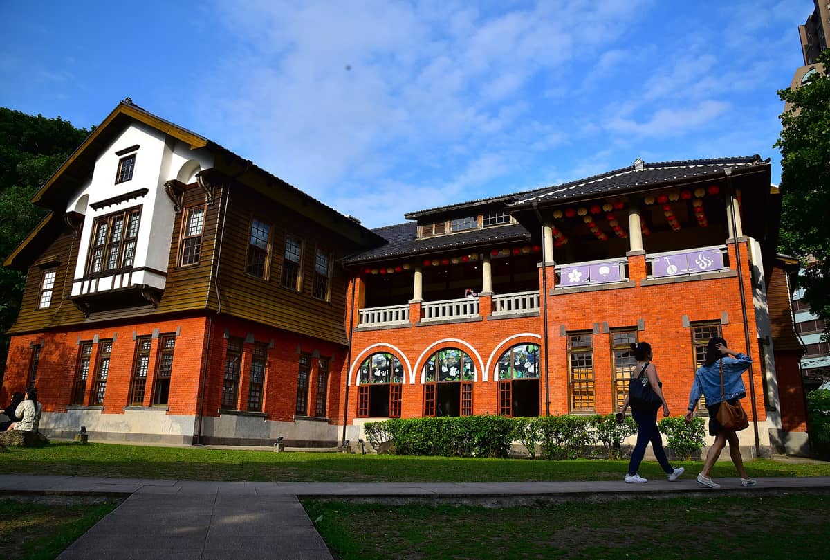 Die Außenansicht des Beitou Heißquellenmuseums – ein beeindruckendes zweistöckiges Gebäude aus rotem Backstein und Holz in Taipei mit Bogenfenstern und Besuchern davor.