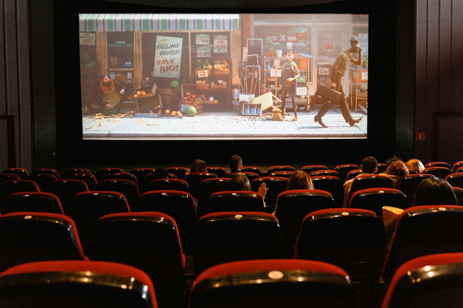 Filas de butacas de terciopelo rojo con personas viendo una película en una gran pantalla en un cine clásico.
