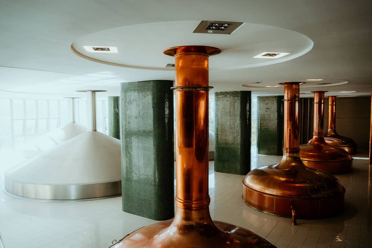 Caldeiras e equipamentos modernos de fabricação de cerveja em uma cervejaria, com reluzentes recipientes de cobre e pisos de azulejo limpos.