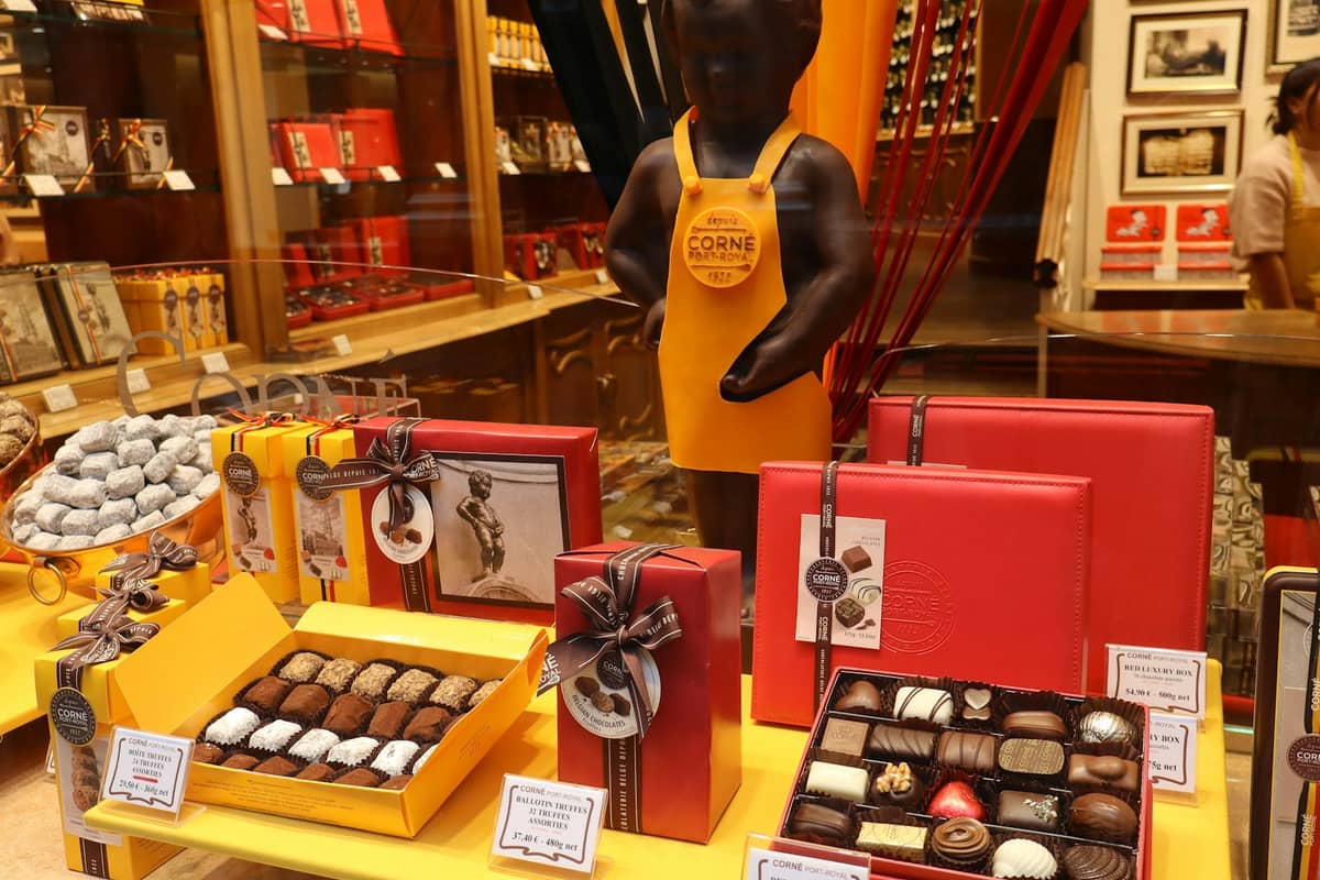 Sortimento de caixas de chocolate belga na vitrine de uma chocolateria em Bruxelas, com a famosa estátua do Manneken Pis ao fundo.