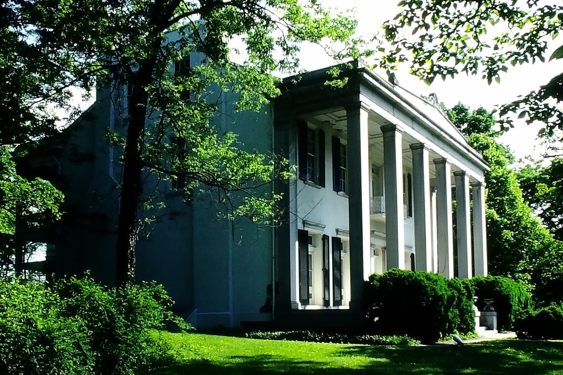 La mansión Belle Meade, un grandioso edificio blanco de estilo Revival Griego con altas columnas, rodeado de exuberantes árboles verdes y jardines cuidadosamente recortados.