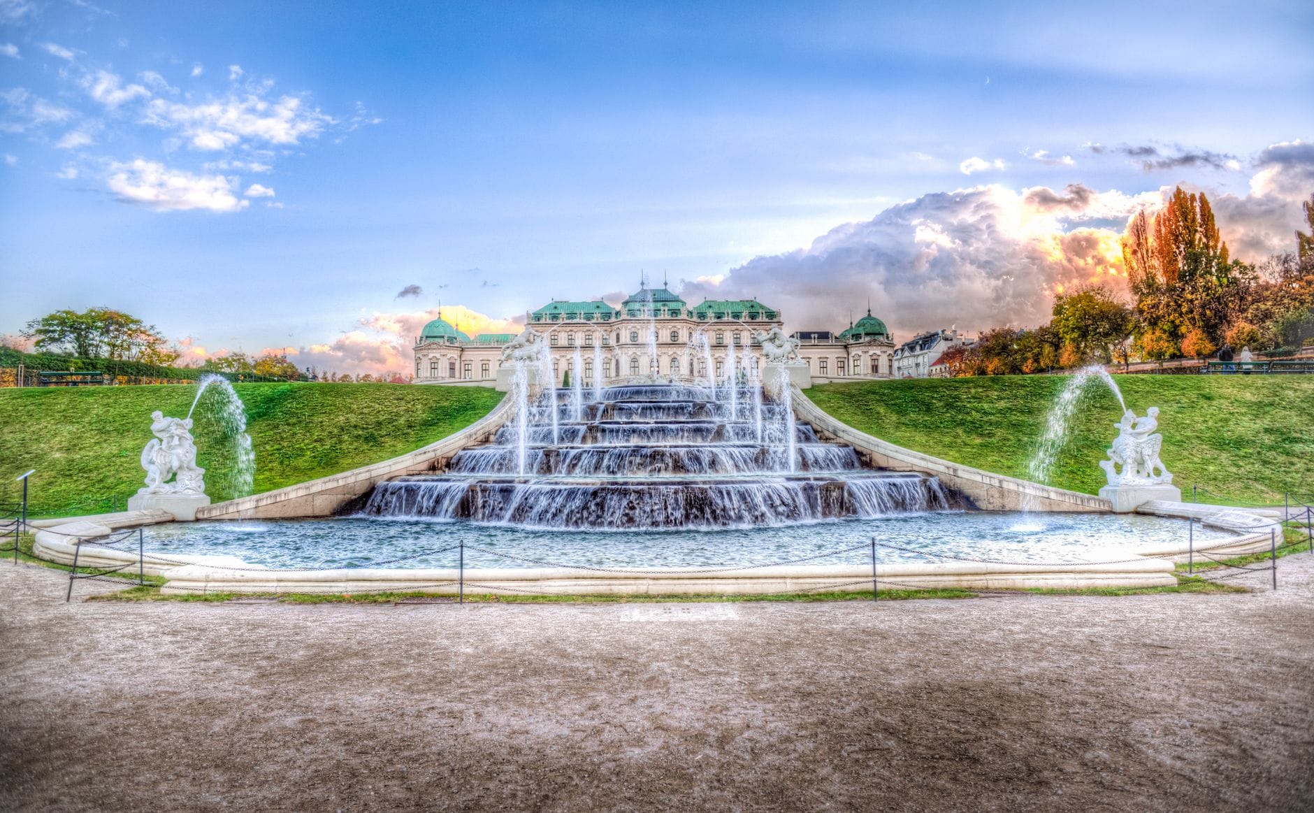 Dramatischer Sonnenuntergang über dem Schloss Belvedere mit gestuften Barockfontänen und gepflegten Gärten in Wien – ein beeindruckendes Bild der Anlage in ihrer ganzen Pracht.