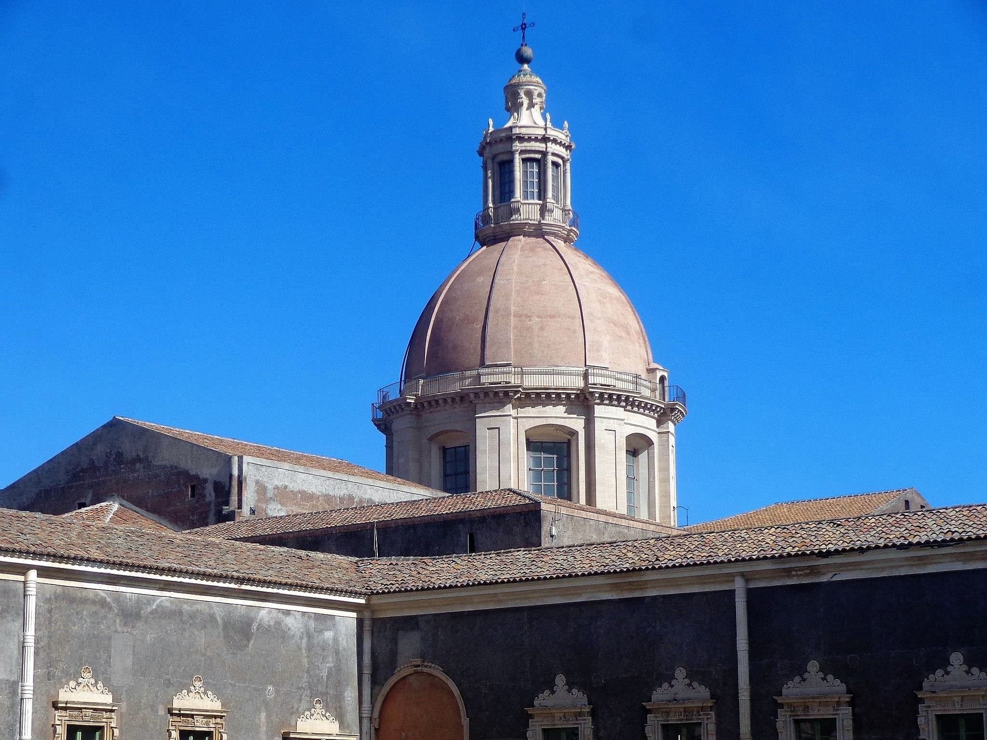 Das gewölbte Dach und die Barockarchitektur des Benediktinerklosters San Nicolò l'Arena unter einem klaren blauen Himmel in Catania.