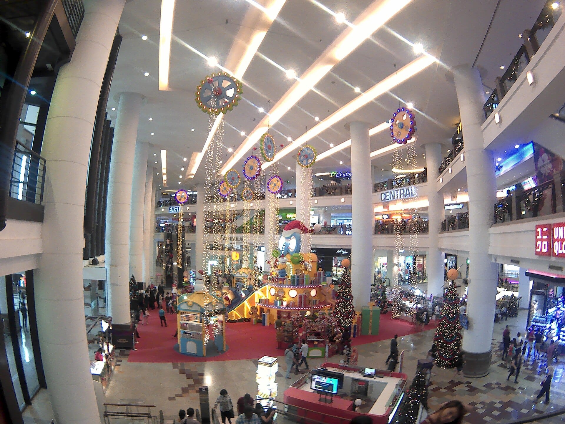 Wide view of Berjaya Times Square's bright, spacious atrium with festive decorations, tall columns, multiple floors, and crowds of shoppers.