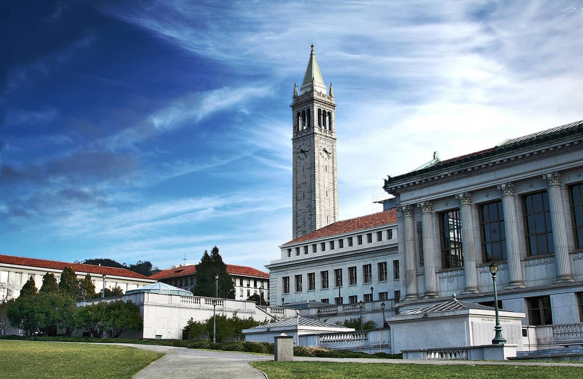 UC Berkeleys Sather Tower und klassische Campusgebäude unter einem strahlend blauen Himmel, mit grünen Rasenflächen und umliegenden Bäumen.