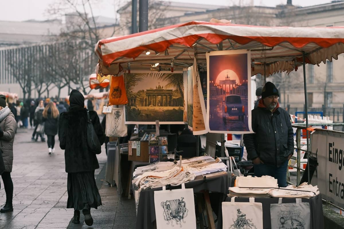 Outdoor-Flohmarktstand in Berlin mit Kunstdrucken, Tragetaschen und Menschen, die in einer Stadtstraße stöbern.