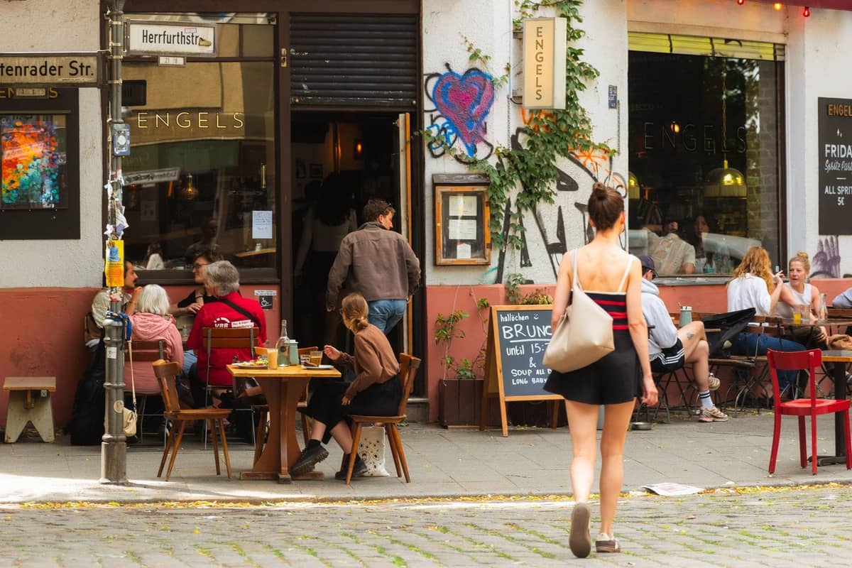 Vista de la calle de un animado café en Berlín con terraza, gente comiendo y grafitis en las paredes, evocando la singular escena gastronómica local de Berlín.