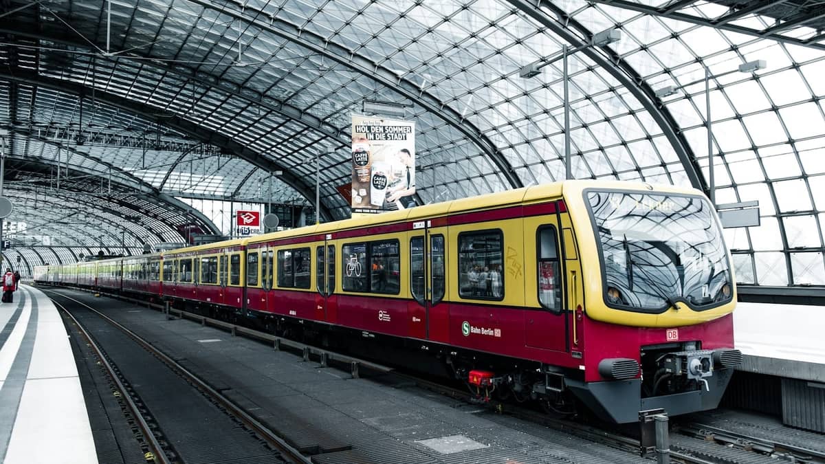 Moderno treno S-Bahn sul binario della Berlin Hauptbahnhof con tetto a volta in vetro e passeggeri in attesa in una giornata luminosa