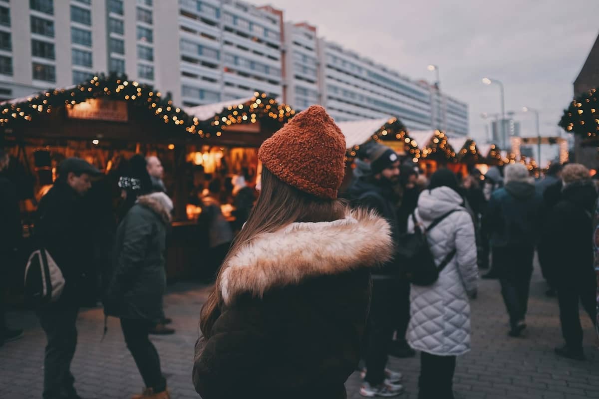 Persone in cappotti invernali che godono del mercatino di Natale di Berlino con luci festive e bancarelle in legno all'aperto.