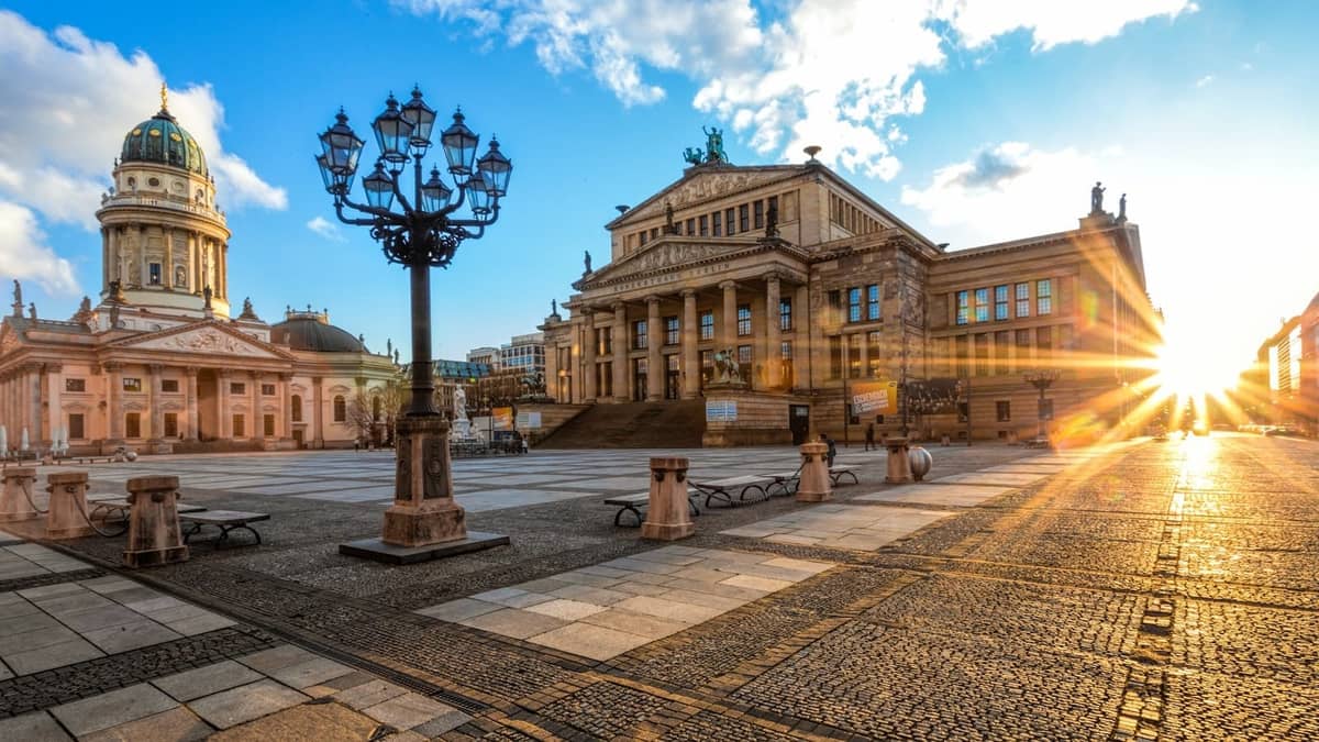 Vista ampia della piazza Gendarmenmarkt al tramonto, con la sala concerti e la cattedrale di Berlino, e lo spazio vuoto dove di solito vengono allestite le bancarelle del mercatino di Natale.