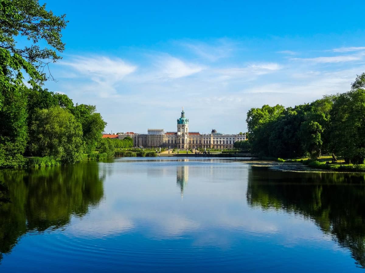 Vista su un lago calmo verso il Palazzo di Charlottenburg a Berlino, con rigogliosi alberi che incorniciano la scena sotto un cielo azzurro luminoso.