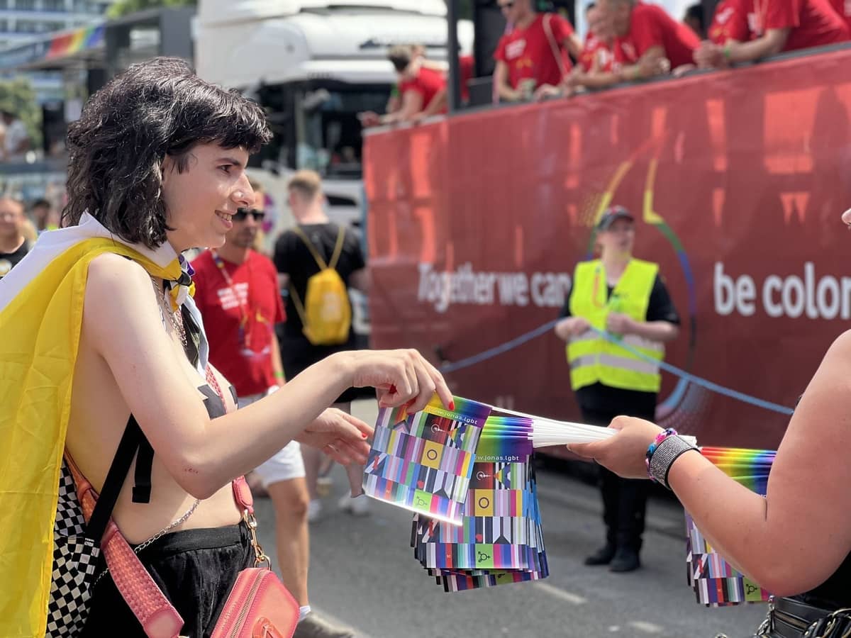 Person mit einer Pride-Flagge verteilt Regenbogen- und Intersex-Flaggen bei einer farbenfrohen Straßenveranstaltung in Berlin.