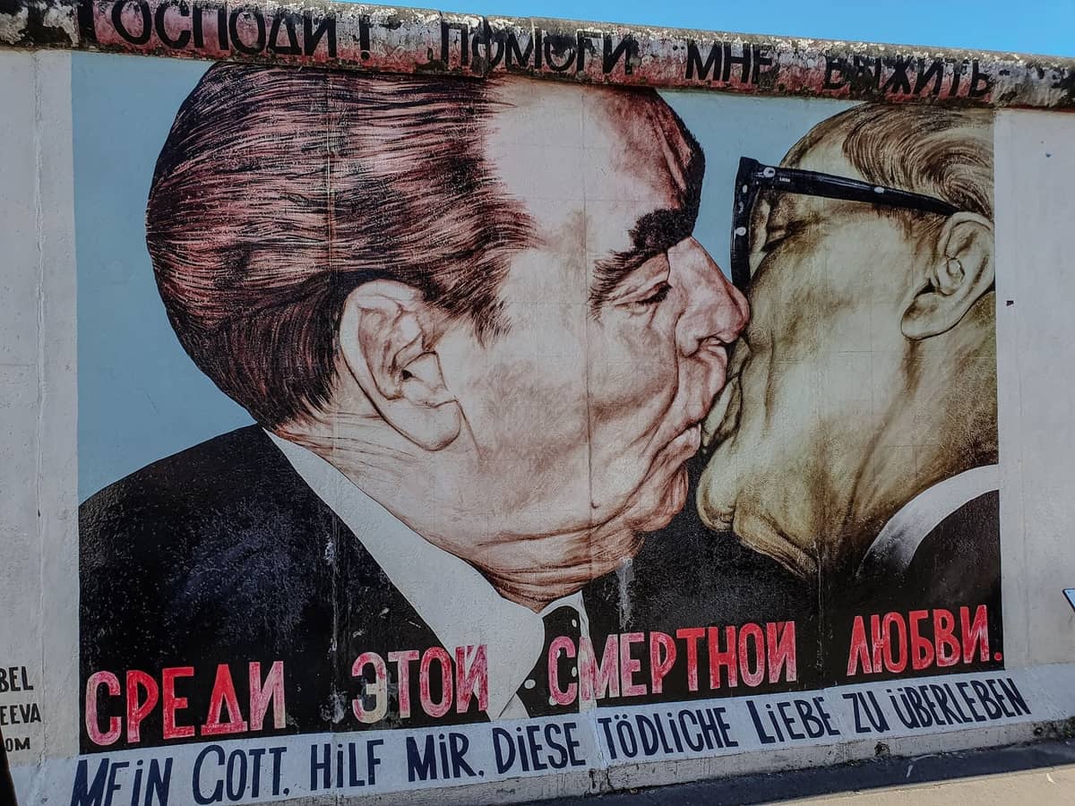 Nahaufnahme des berühmten Wandgemäldes zweier sich küssender Männer auf einem erhaltenen Abschnitt der Berliner Mauer unter blauem Himmel.