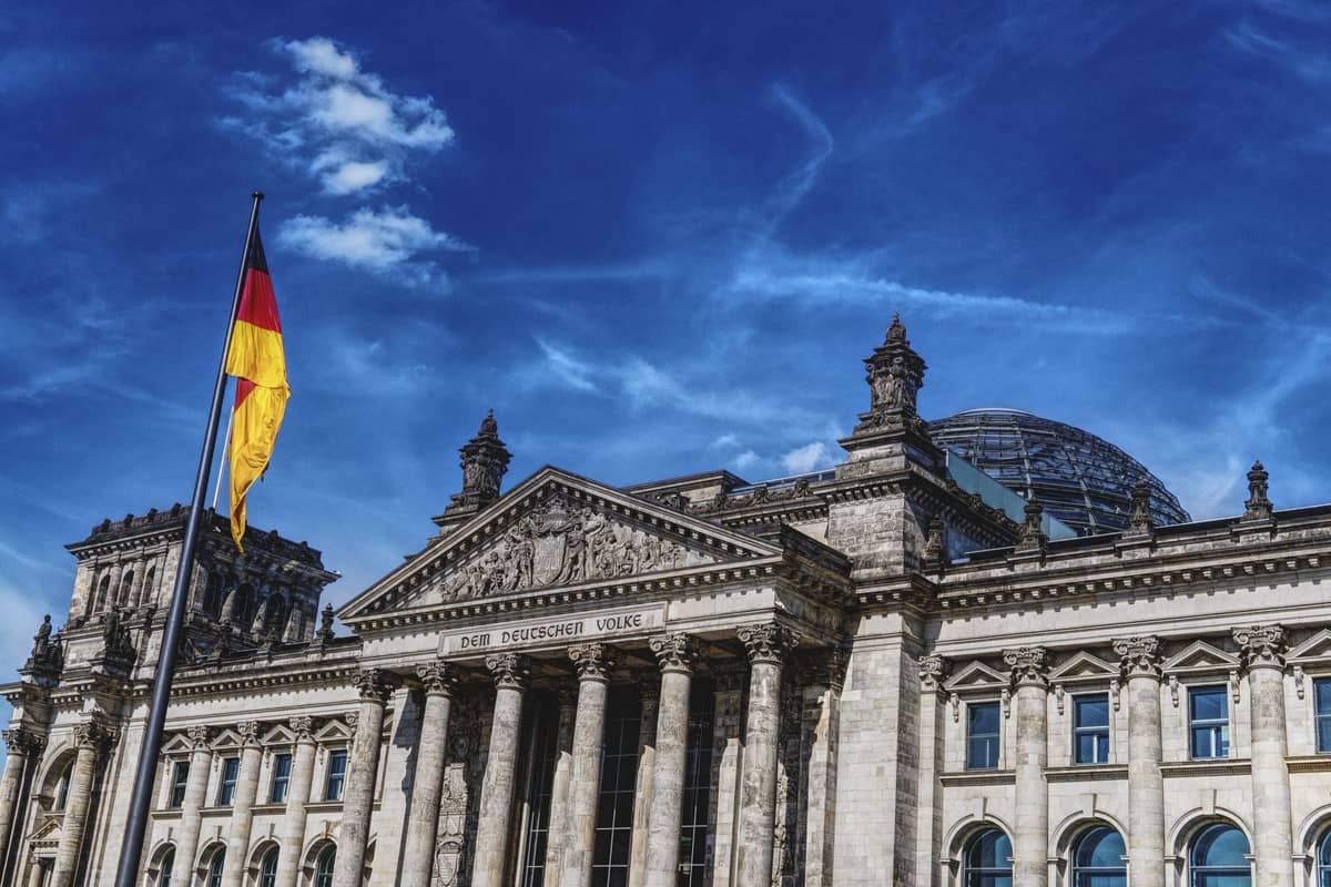 Das Reichstagsgebäude in Berlin mit deutscher Flagge und Glaskuppel unter einem leuchtend blauen Himmel, Symbol der deutschen Geschichte und Identität.