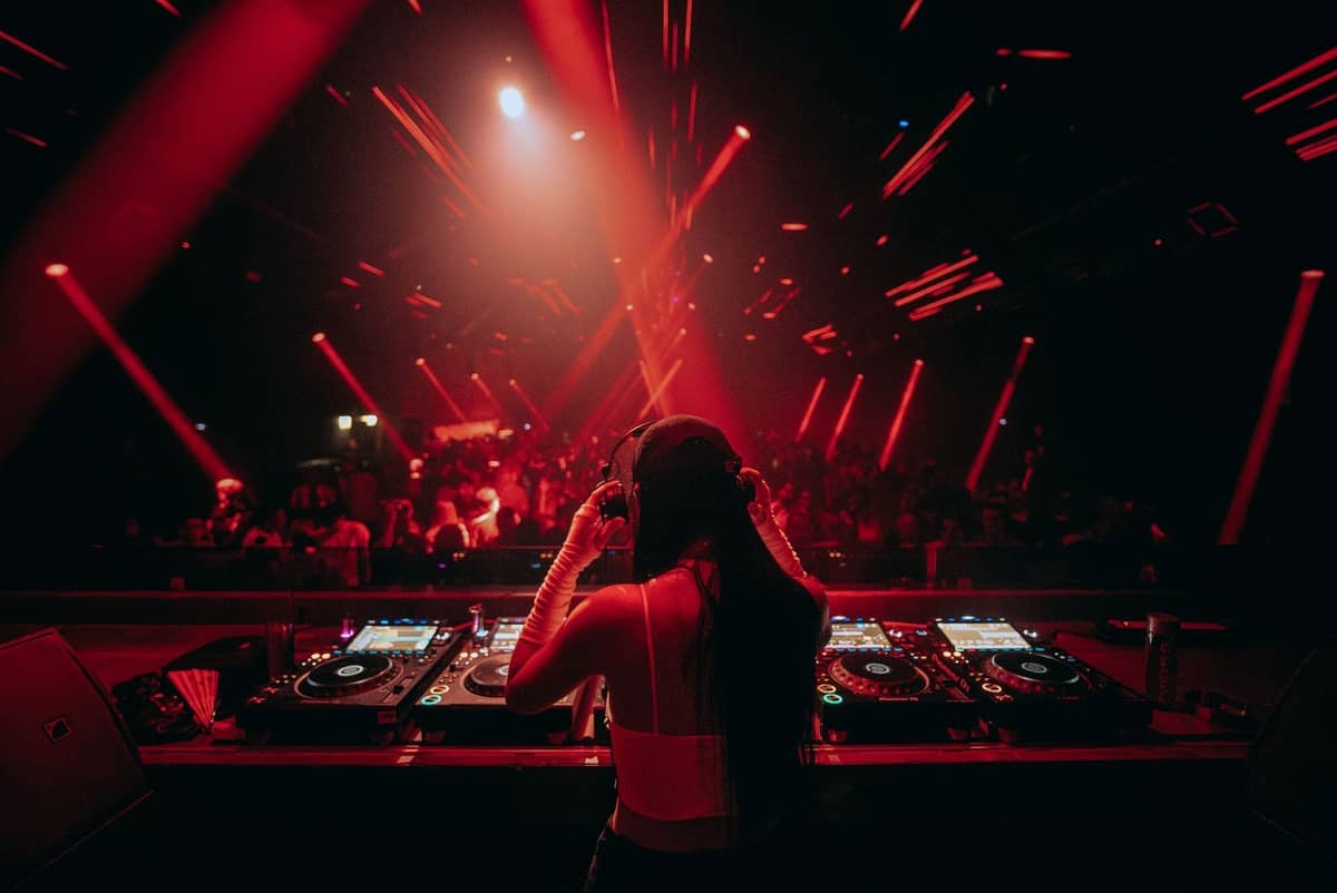 DJ występujący w klubie z czerwonym oświetleniem, widok zza stanowiska DJ-a, zatłoczony parkiet w tle