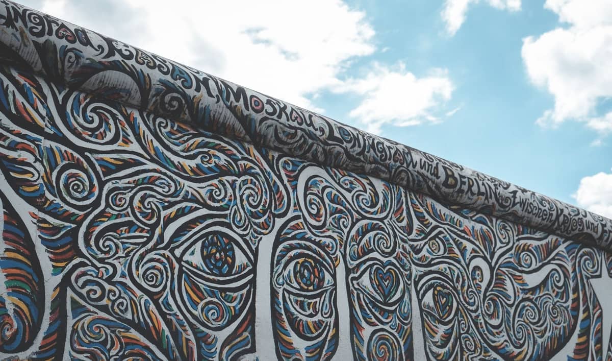 Kısmen bulutlu bir gökyüzünün altında canlı, girdaplı grafiti sanatıyla kaplı Berlin Duvarı'nın bir bölümü.