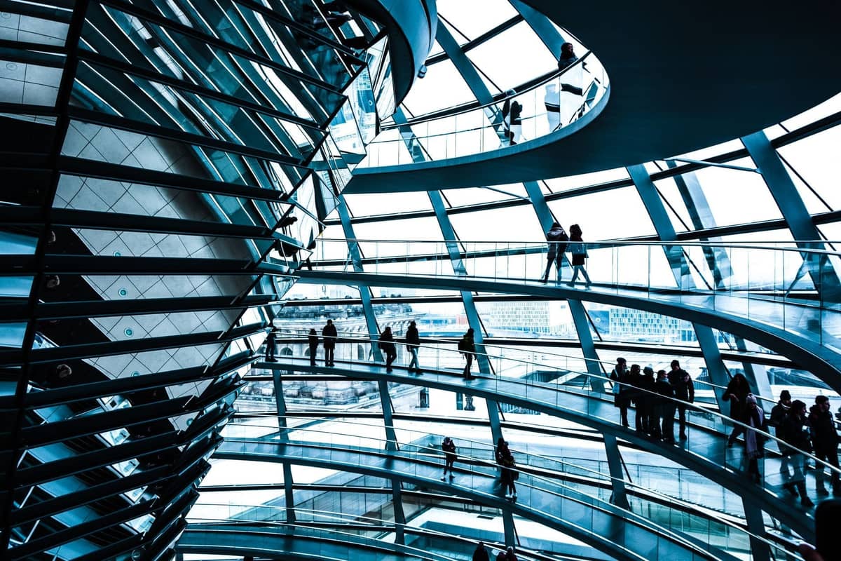 Widok wnętrza kopuły Reichstagu w Berlinie z wieloma zwiedzającymi spacerującymi po spiralnych rampach i podziwiającymi architekturę oraz panoramę miasta.