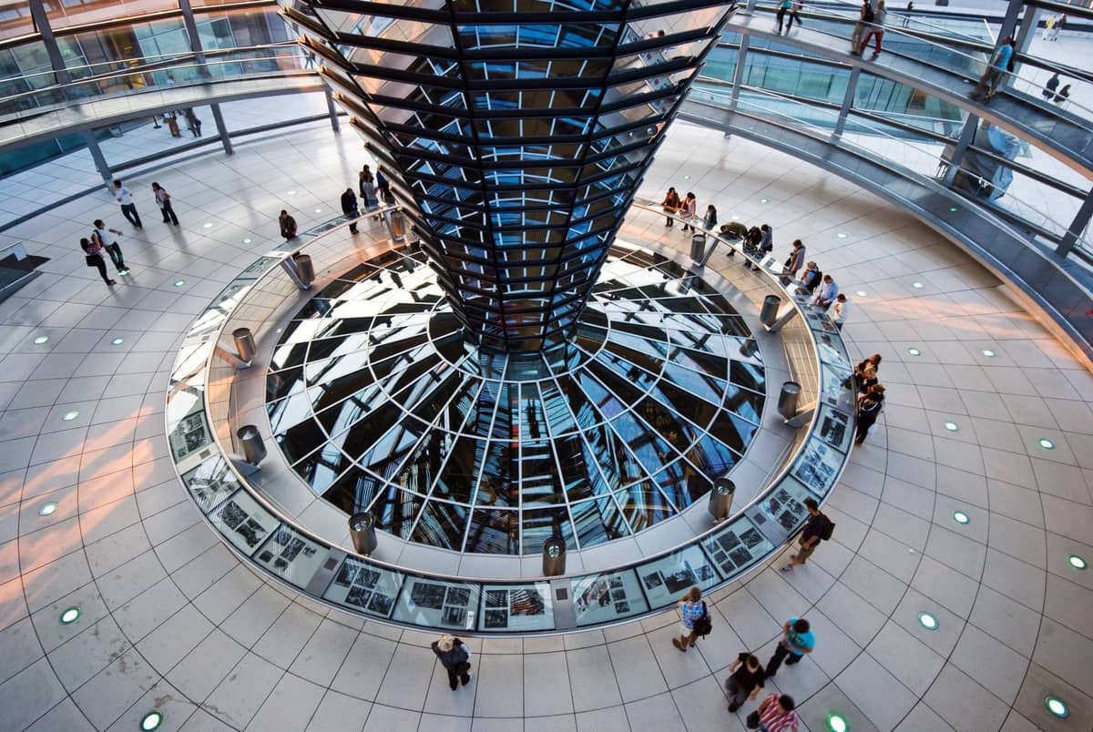 Widok z wnętrza kopuły Reichstagu przedstawiający spiralne rampy, lustrzany lejek i zwiedzających eksplorujących okrągłą ścieżkę.