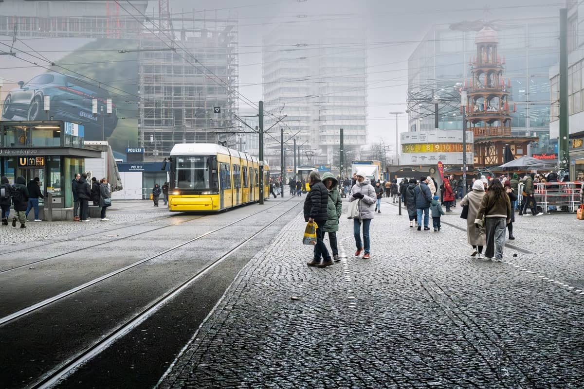 Belebter Stadtplatz in Berlin mit Menschen, die spazieren gehen, einer gelben Straßenbahn und modernen Gebäuden, typisch für touristisch geprägte Gebiete mit erhöhtem Taschendiebstahlrisiko.