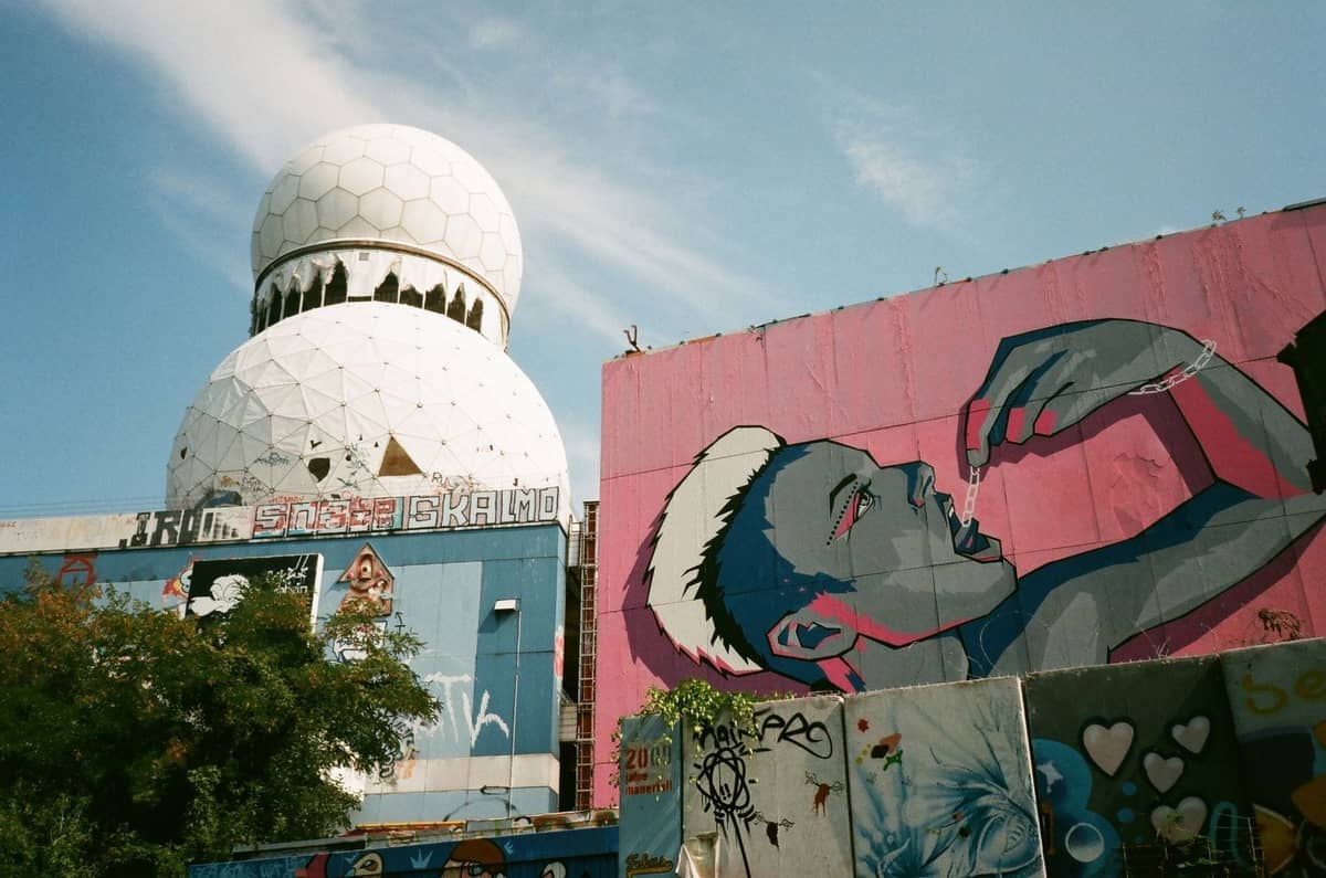 Ikonische Teufelsberg-Kuppeln und ein großes buntes Wandbild an einer Mauer in einer offenen, sonnigen Szene an Berlins verlassener Abhörstation.