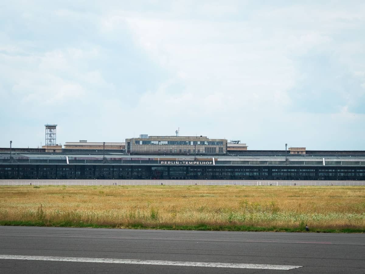 Vista amplia del edificio del aeropuerto Berlin Tempelhof con su letrero visible a través de un campo abierto de hierba y asfalto.