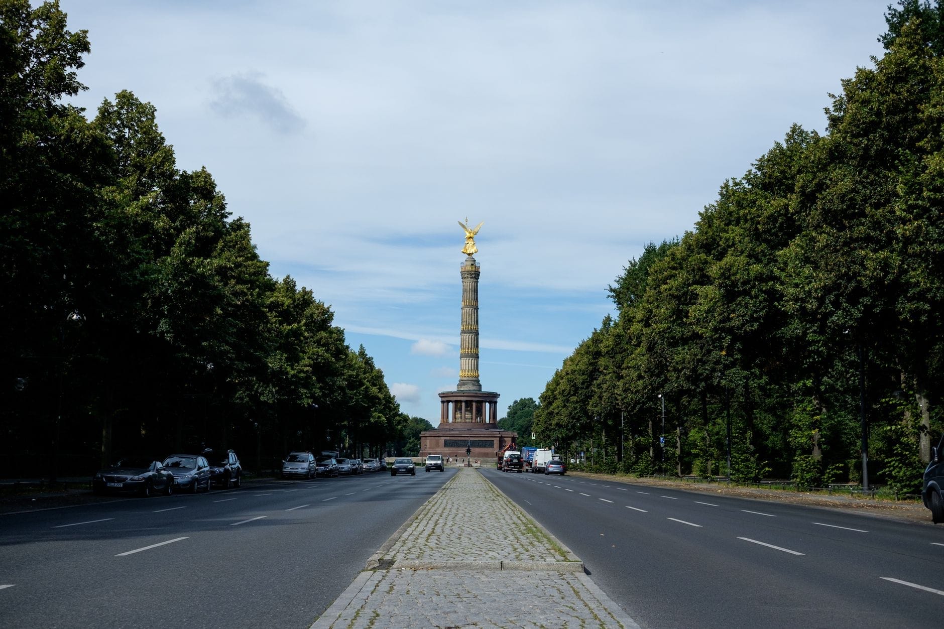 Vista ampia sul viale alberato che conduce alla Colonna della Vittoria di Berlino, con la sua statua dorata, sotto un cielo azzurro nel parco del Tiergarten.