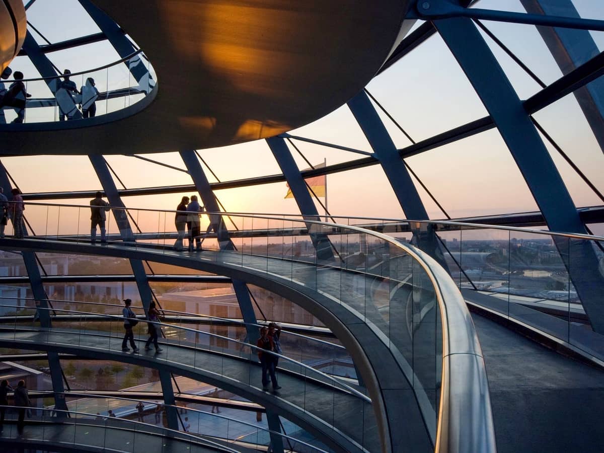 Menschen, die bei Sonnenuntergang in der Kuppel des Reichstags in Berlin spazieren, mit Panorama-Glasaussicht und moderner Architektur.