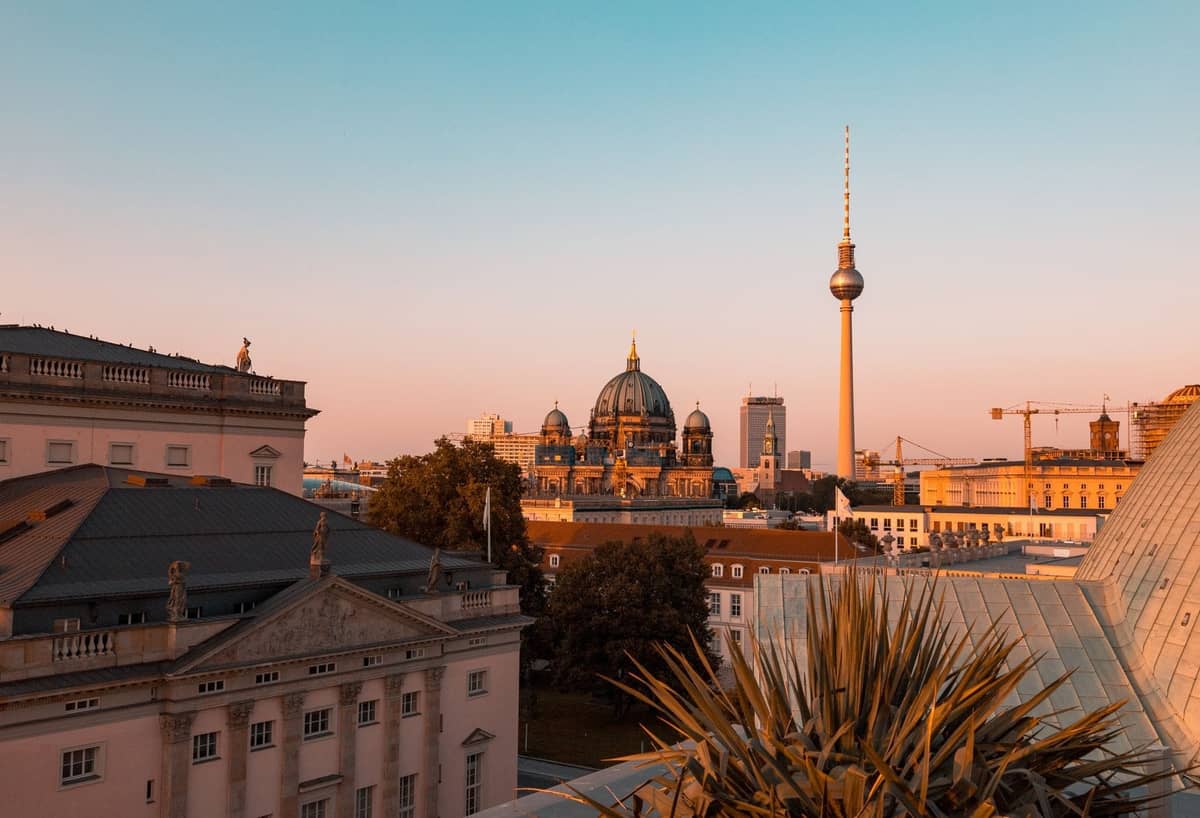 Dachterrassen-Blick über Berlin bei Sonnenuntergang mit Fernsehturm und Berliner Dom, aufgenommen von einer hohen Terrasse, mit Pflanzen im Vordergrund.