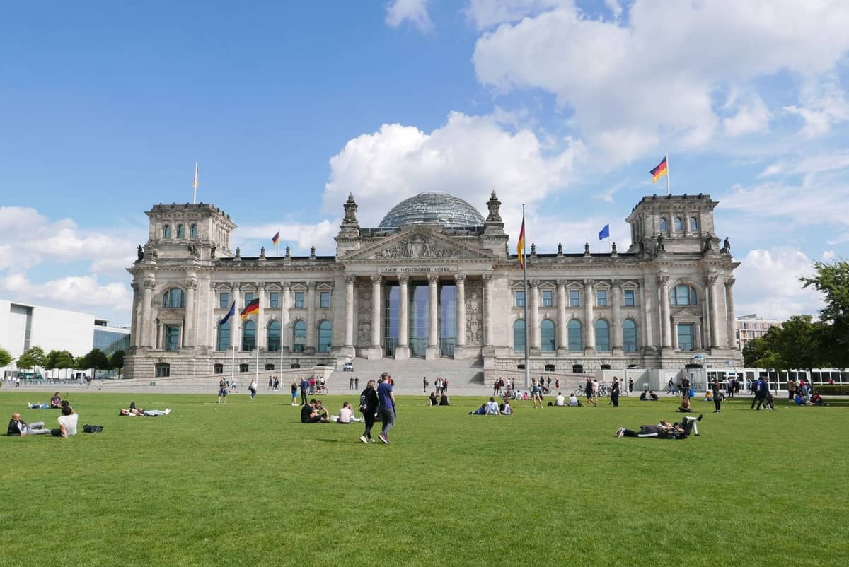 Weitwinkelansicht des Reichstagsgebäudes mit Menschen, die sich auf dem grünen Rasen unter blauem Himmel entspannen und spazieren gehen, Berlin.