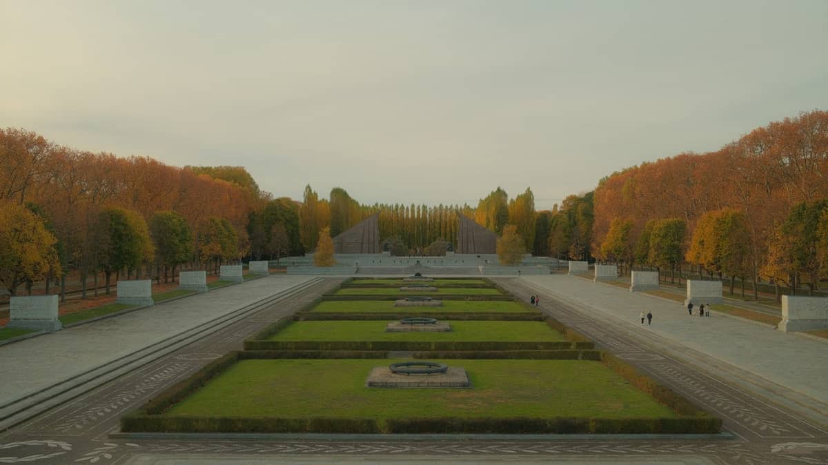 Weitwinkelansicht des Sowjetischen Ehrenmahls im Treptower Park in Berlin mit baumgesäumten Wegen und grünen Rasenflächen im Herbst.