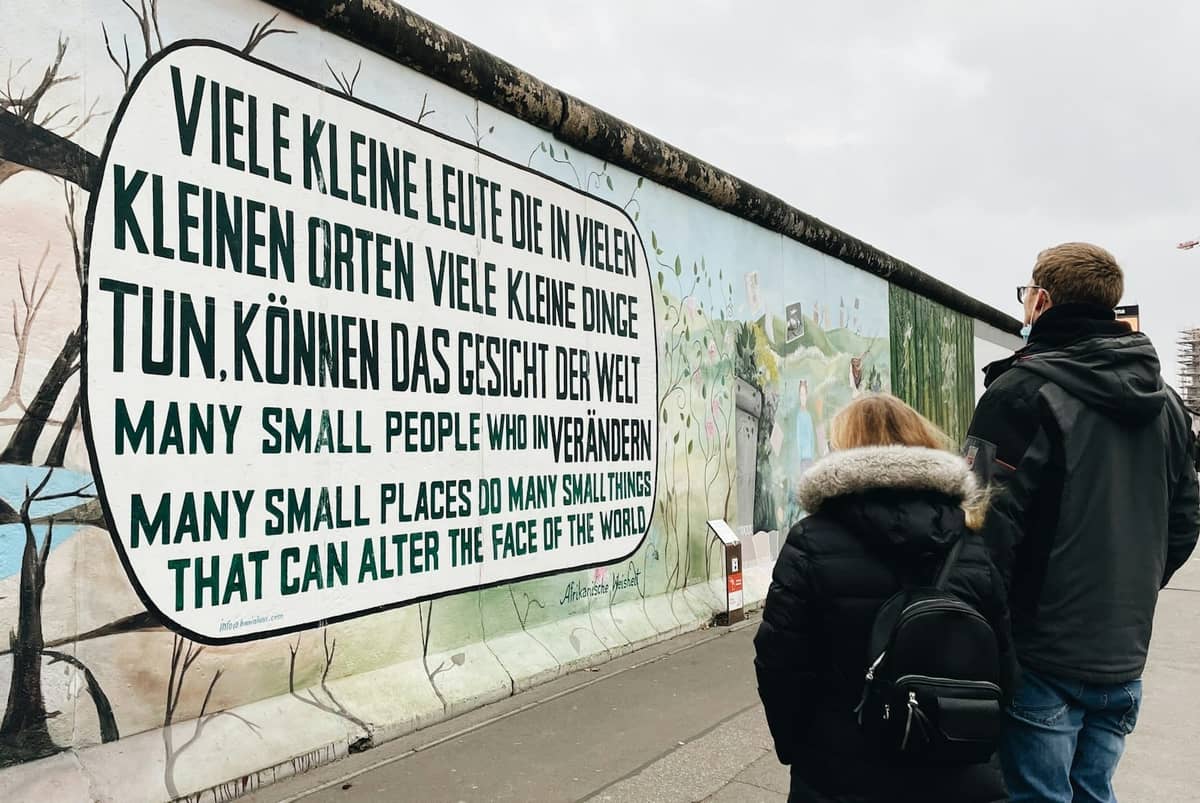 Besucher betrachten ein berühmtes Wandgemälde an der Berliner Mauer in der East Side Gallery mit einer mehrsprachigen Friedensbotschaft.
