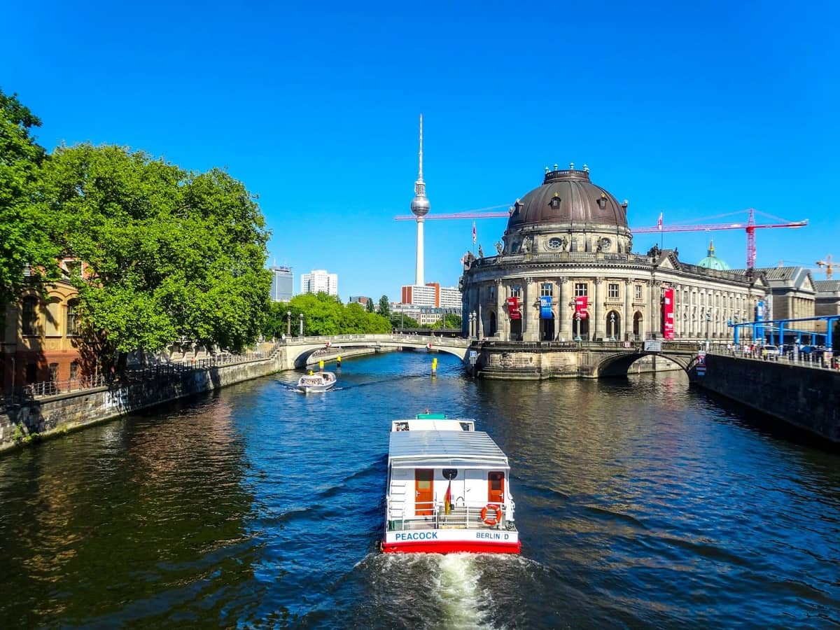Vista luminosa y soleada del Bode Museum de Berlín con la Torre de TV y un barco turístico en el río Spree, capturando los icónicos atractivos de Berlín.