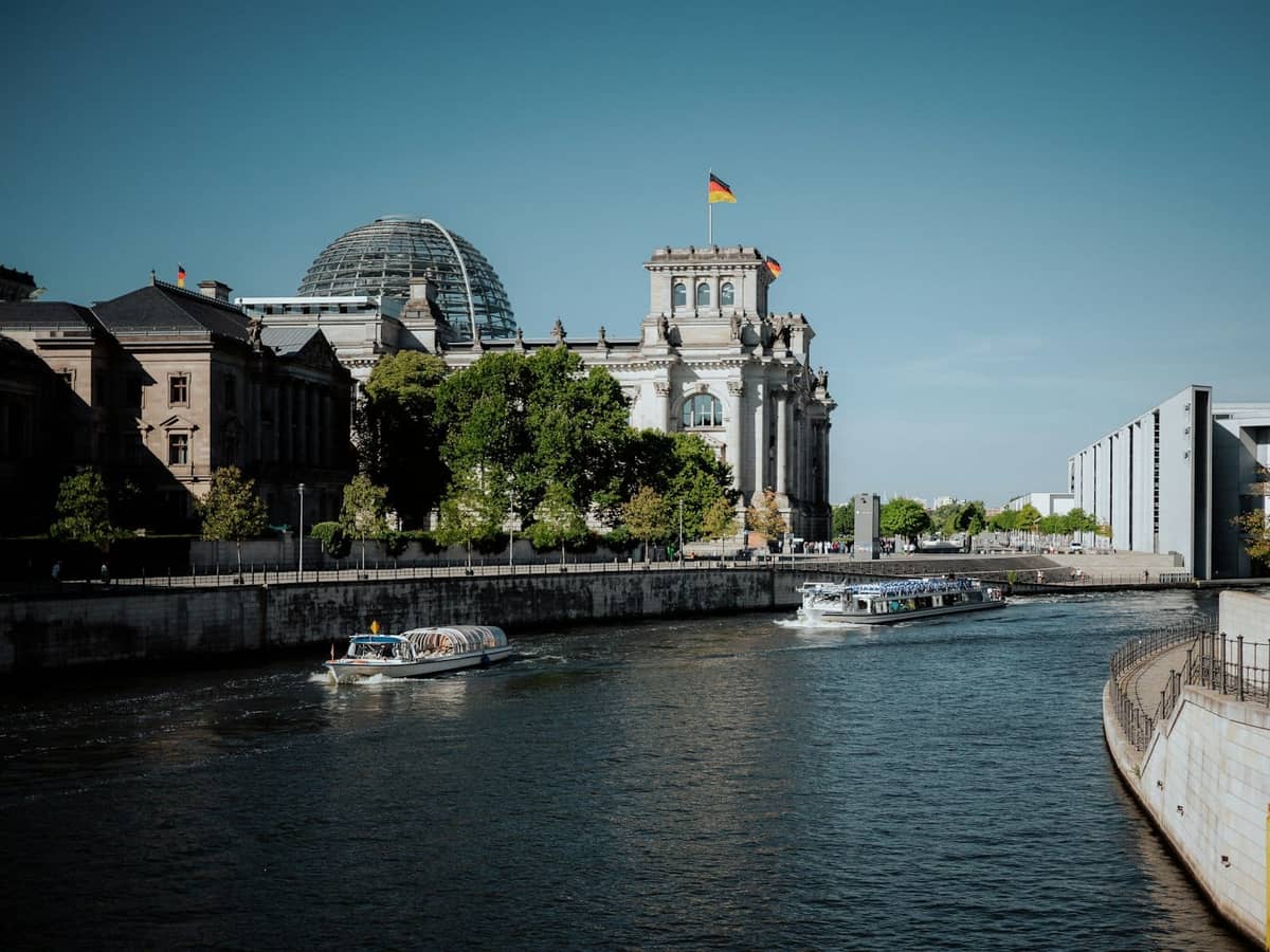 El río Spree en Berlín con barcos en el agua y el edificio del Reichstag al fondo bajo un cielo despejado de verano.