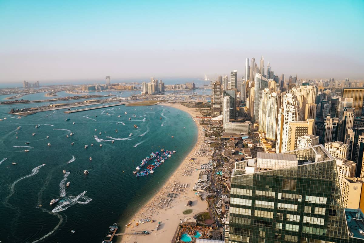 Luftaufnahme eines Stadtstrandes in Dubai mit sandiger Küstenlinie, Sonnenbadenden und Hochhäusern entlang der Küste.