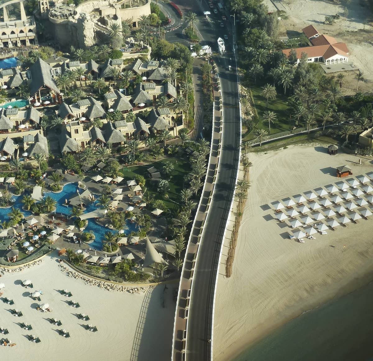 Luftaufnahme des Wild Wadi Wasserparks in Dubai mit blauen Pools, Palmen und angrenzendem Privatstrand mit Liegestühlen und Sonnenschirmen.