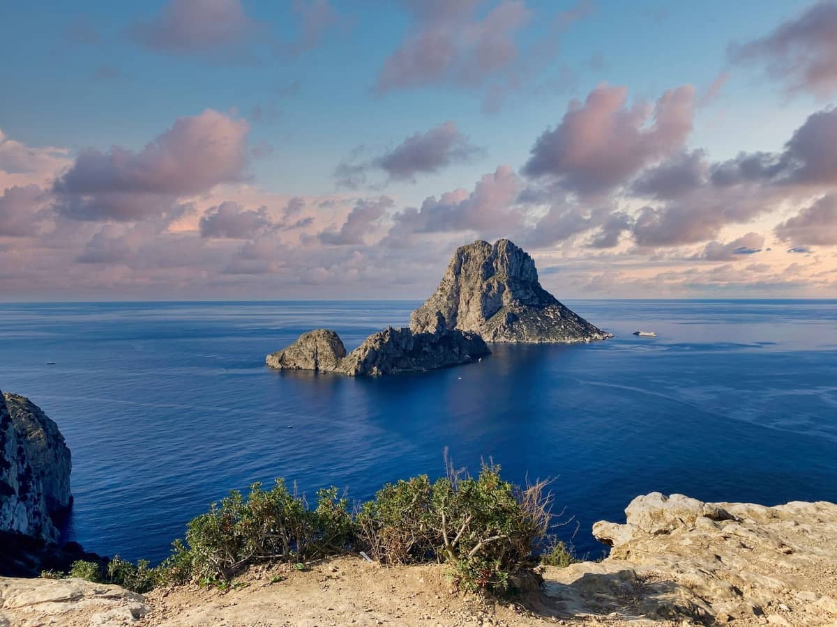Dramatic rocky coastline with Es Vedrà island rising from the sea under a colorful sky in southwest Ibiza.