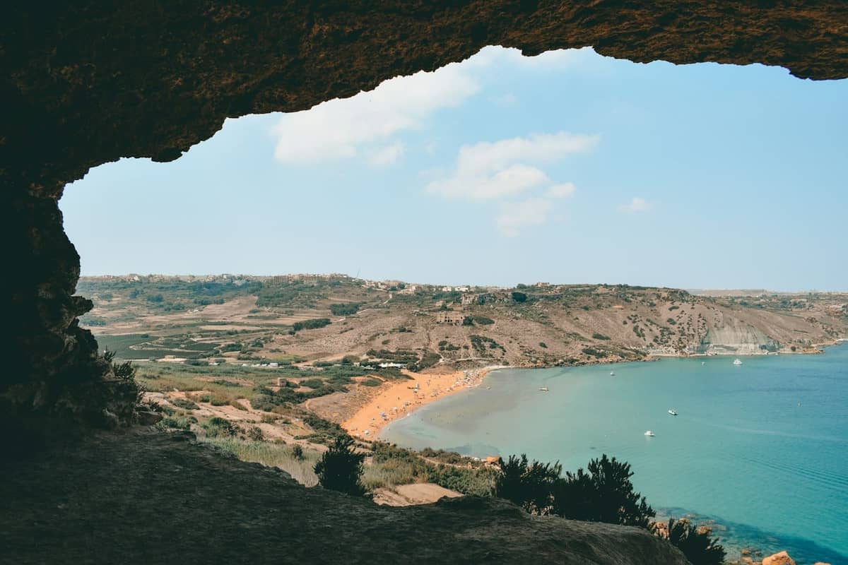 Vista della spiaggia dall'interno di una grotta con sabbia dorata, acqua blu cristallina e scogliere frastagliate a Gozo, Malta