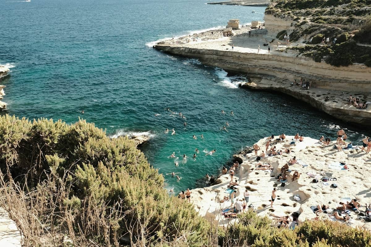 Persone che prendono il sole e nuotano intorno a lastre piatte di calcare e piscine naturali nella roccia su una costa maltese.