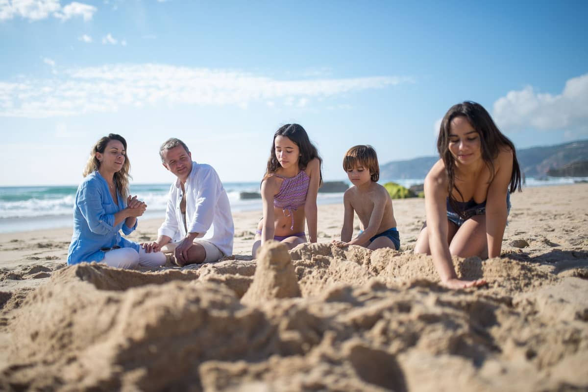 ครอบครัวที่มีเด็กๆ ร่วมกันสร้างปราสาททรายบนชายหาดที่แดดสดใส มีคลื่นและท้องฟ้าสีฟ้าเป็นฉากหลัง