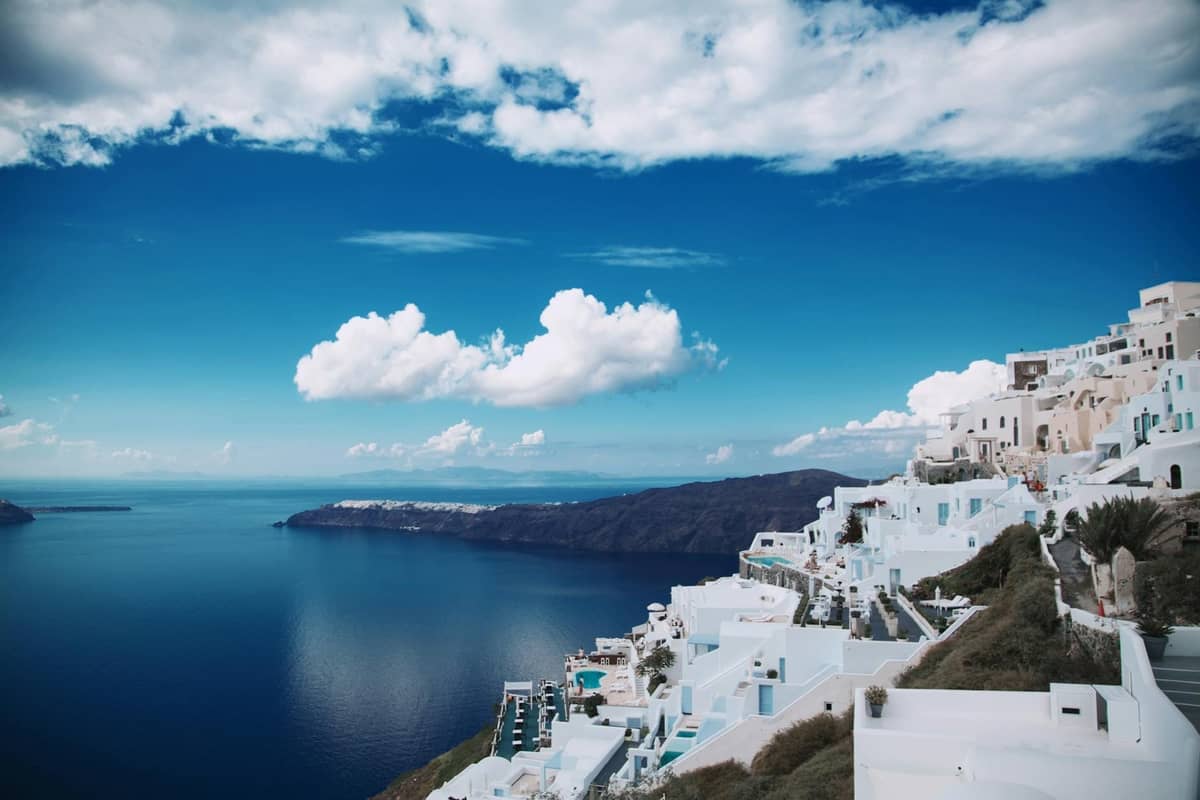 Splendida vista dalla scogliera su edifici bianchi che si affacciano sul mare blu profondo e sulla caldera di Santorini in una giornata limpida e soleggiata.