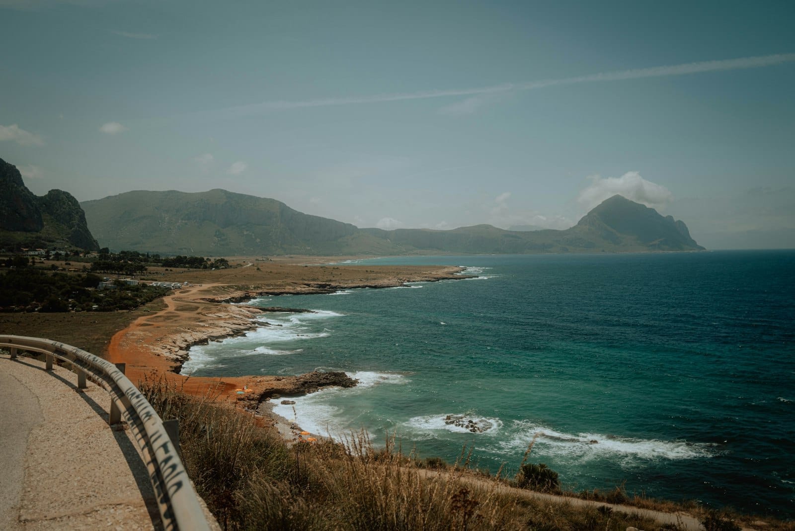 Kurvenreiche Küstenstraße über türkisfarbenem Meer, mit dramatischen Kalksteinbergen und zerklüfteter Küstenlinie, typisch für Siziliens tyrrhenische Nordküste.