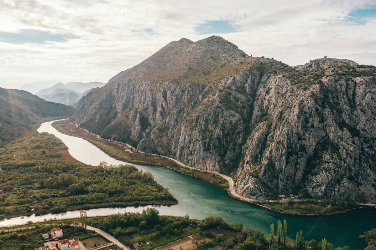 Ein breiter Fluss schlängelt sich durch eine beeindruckende grüne Schlucht mit steilen Felsklippen und einer Gebirgslandschaft unter einem teils bewölkten Himmel.