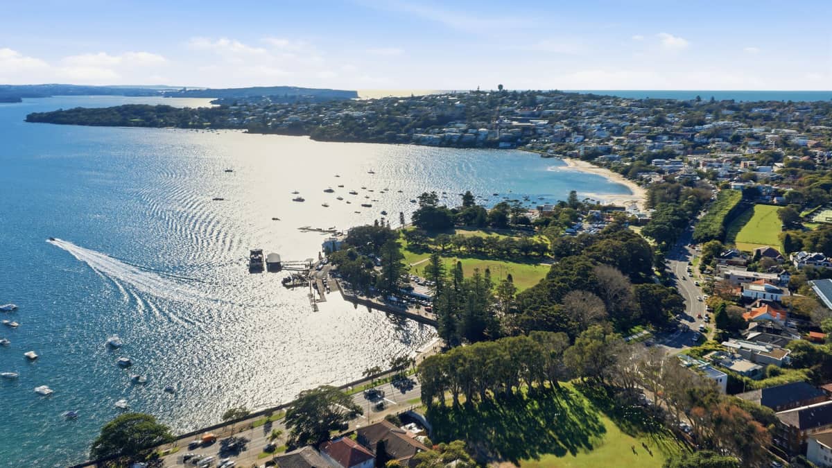 Vista aérea de una playa de arena y una cala protegida rodeada de barcos, árboles y casas residenciales en Sydney Harbour.