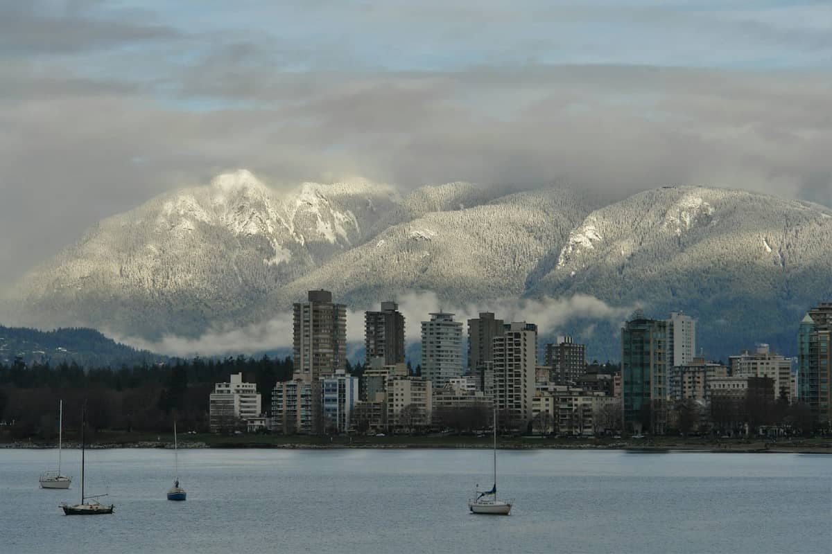 เส้นขอบฟ้าของ Vancouver พร้อมริมน้ำ เรือใบ และภูเขาที่ปกคลุมด้วยหิมะในพื้นหลังในวันที่มีเมฆมาก