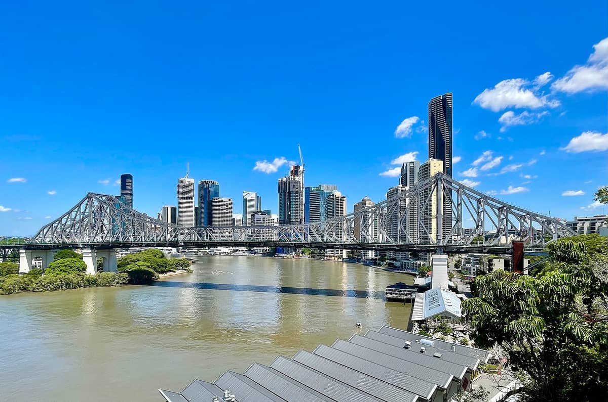 Brisbane city skyline with Story Bridge crossing the Brisbane River under a clear blue sky, illustrating the city’s riverfront location and lack of beaches in the CBD.