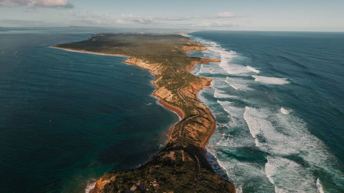 Widok z lotu ptaka na krętą drogę nadmorską wzdłuż skalistego wybrzeża z falami rozbijającymi się o brzeg Mornington Peninsula, od strony oceanu.