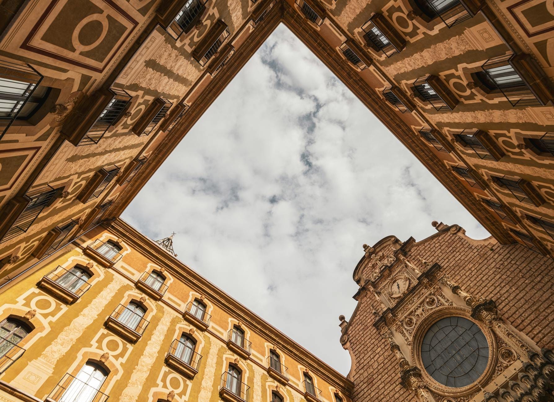 Façade d'église baroque à Naples encadrée par des bâtiments ocre richement décorés sous un ciel nuageux, vue depuis un angle dramatique en contre-plongée.