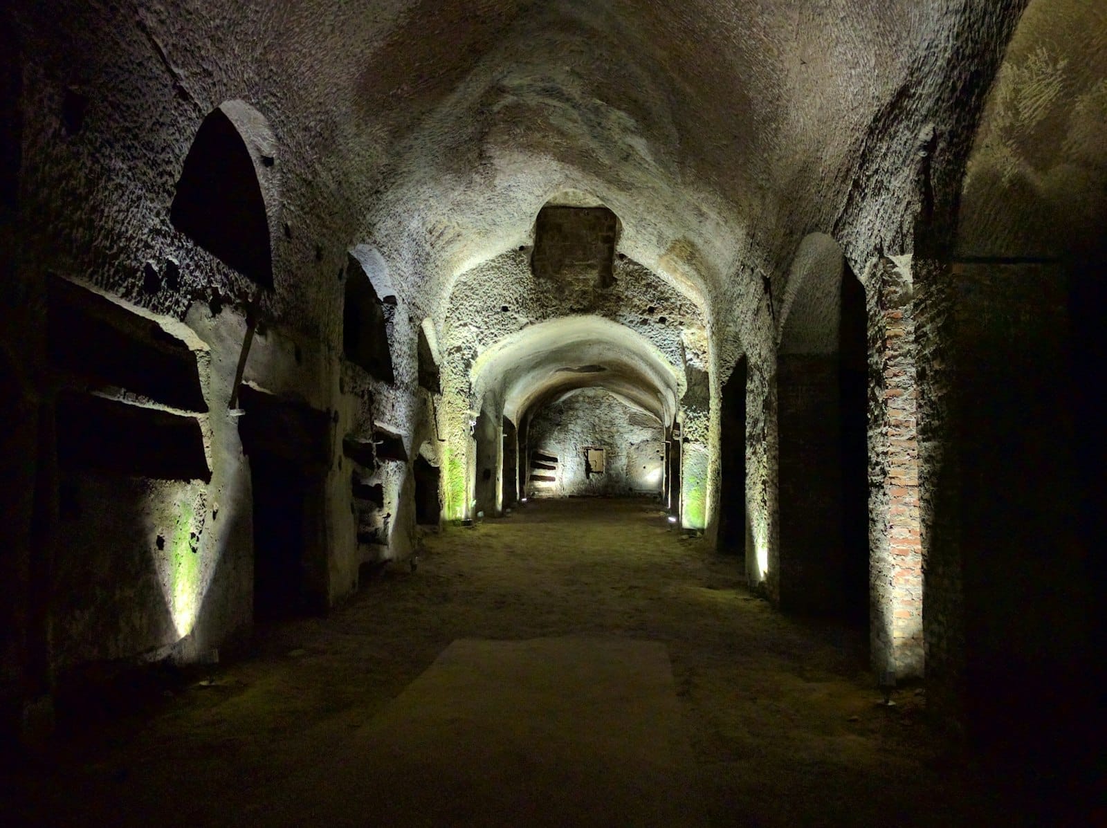 Catacombes souterraines voûtées avec des niches funéraires taillées dans la pierre, doucement éclairées, typiques des complexes d'églises souterraines historiques de Naples.